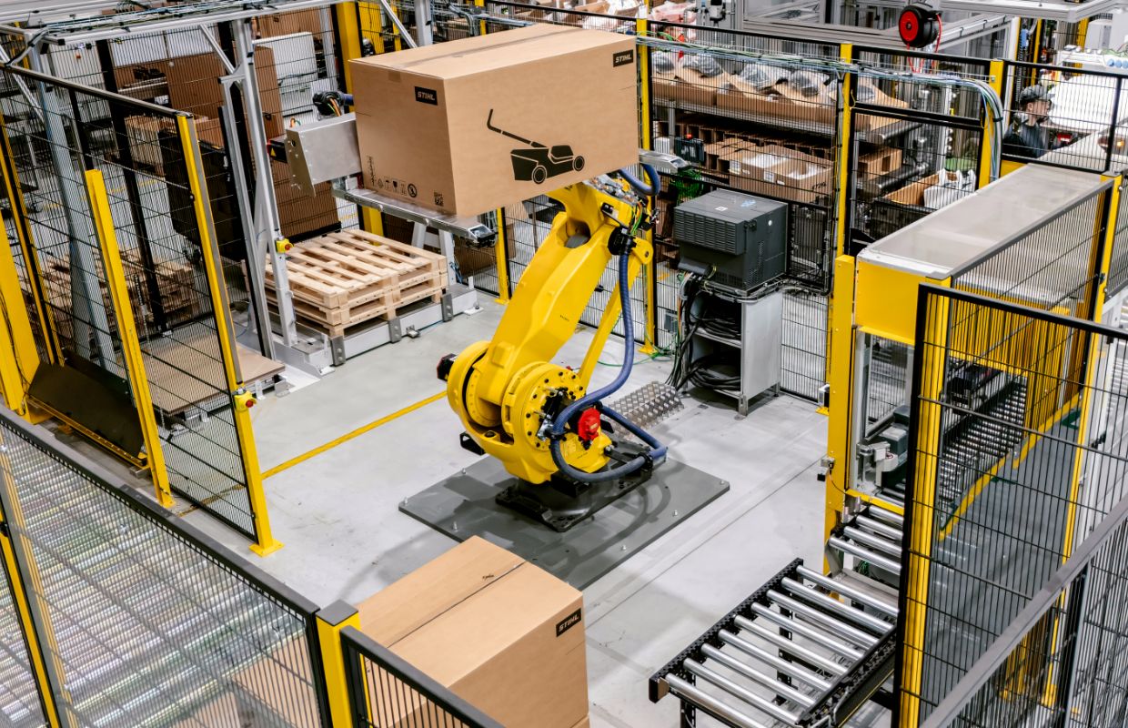 Blick von oben auf eine Verpackungsstation mit Rasenmähern. In der Mitte steht ein Roboter.