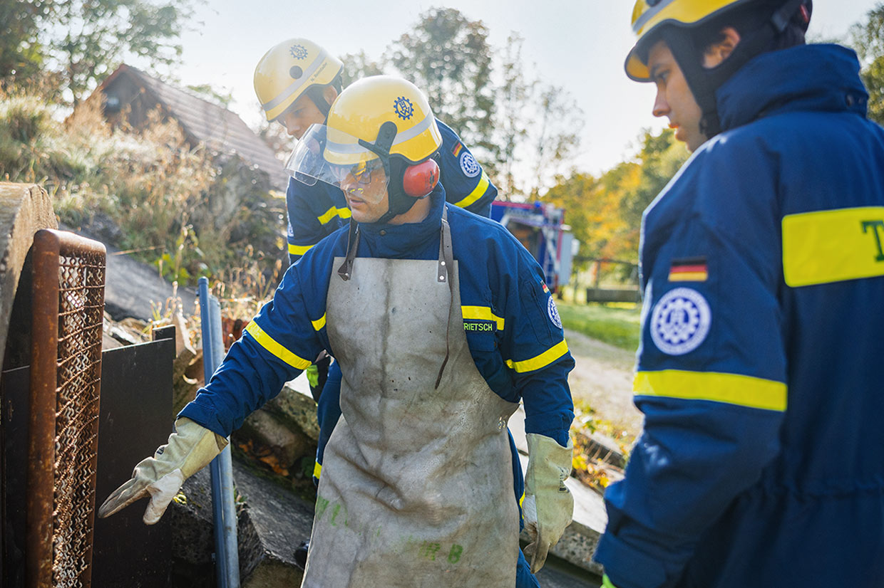 Drei Männer in THW-Uniform stehen um ein Metallgitter und besprechen, wie es optimal durchzuschneiden ist.
